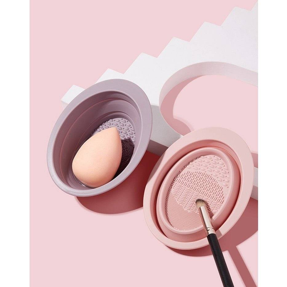 Accesoriu din silicon pentru curățarea pensulelor și bureților de machiaj, prezentat cu un burete cosmetic și o pensulă.