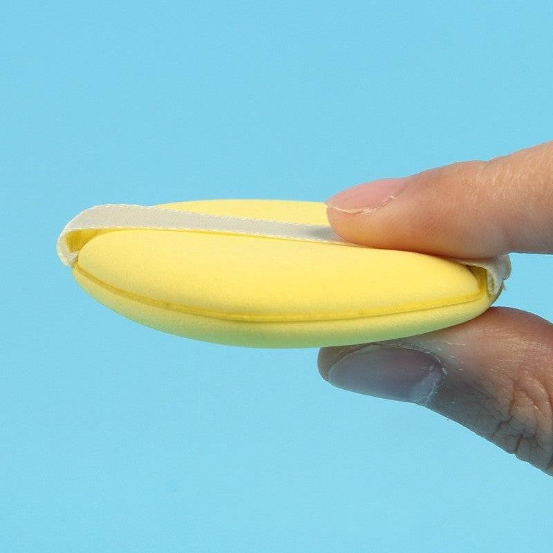 Burete de machiaj galben, subțire și flexibil, ținut între degete. Perfect pentru aplicarea precisă a produselor cosmetice.