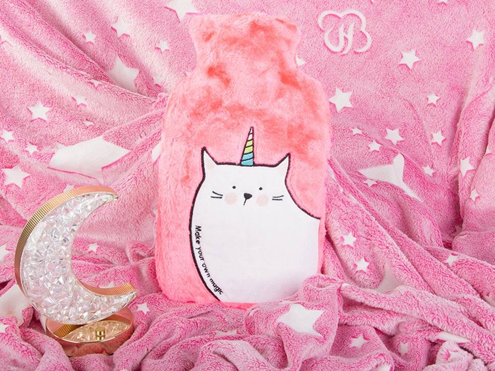Termofor din cauciuc cu husă din pluș roz, așezat pe o pătură pufoasă cu stele. Accesoriu ideal pentru relaxare și căldură.