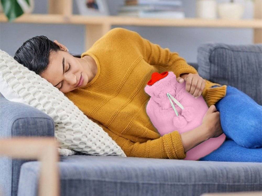 Femeie relaxată pe canapea folosind termoforul mare 1.7L cu husă din pluș moale roz, ideal pentru confort și căldură în zilele reci.